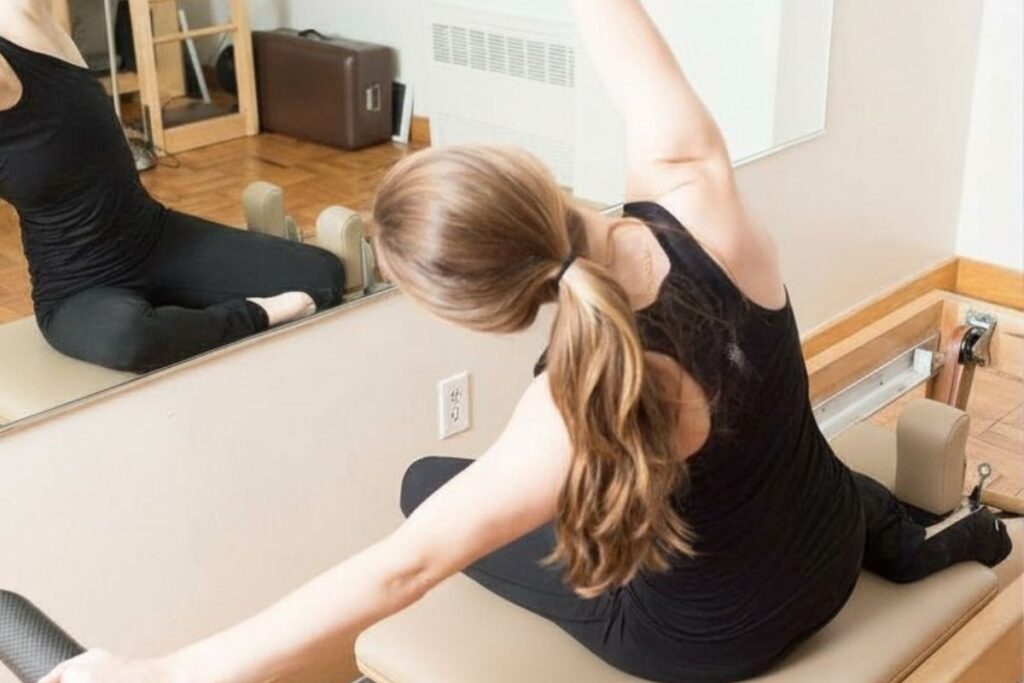 Woman is performing Mermaid on the Reformer during a small group Pilates class